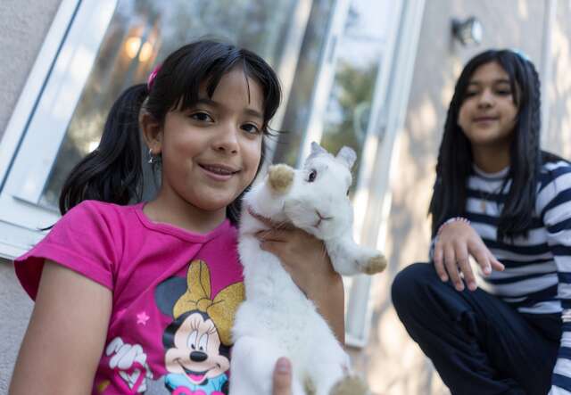 A girl holds up her pet bunny and poses for a photo.