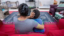 Angelina, an asylum seeker from Guatemala, sits on a red couch with her arms around her son at an IRC Welcome Center in Arizona.