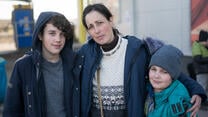 A woman looks at the camera with her arms around her two sons. All are wearing winter clothes.